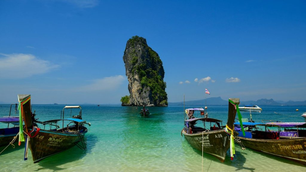 Longtail boats on turquoise water near a limestone island